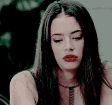 a woman with long dark hair and red lips is wearing a necklace