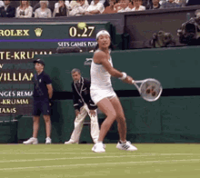 a woman in a white dress is swinging a tennis racquet on a tennis court while the scoreboard says 0.27