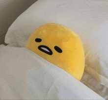 a stuffed yellow egg is laying on a white blanket