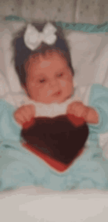 a baby with a bow on her head is holding a heart in her hands