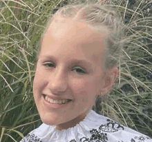 a young girl is smiling for the camera while standing in the grass .