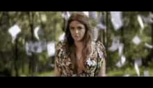 a woman in a floral dress is standing in front of a bunch of papers falling from the sky .