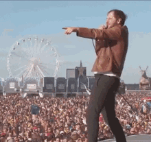 a man singing into a microphone in front of a crowd with a ferris wheel in the background that says drinks