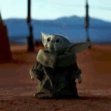 a baby yoda from star wars is standing in the dirt in the desert .