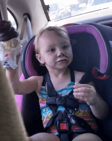 a little girl is sitting in a car seat holding a chocolate ice cream cone