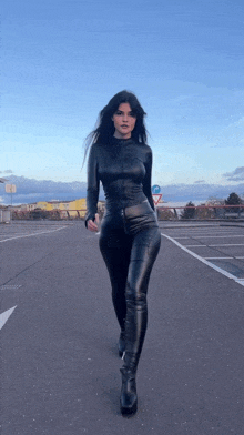 a woman in a black leather outfit is walking down a parking lot