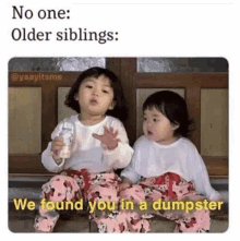 two little girls are sitting next to each other on a bench . one of the girls is holding a bottle of milk .