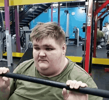 a man in a green shirt is lifting a barbell in a gym with a machine that says precor on it