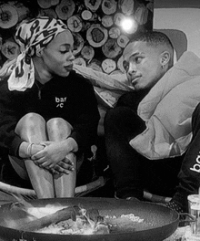 a black and white photo of a man and a woman sitting next to each other with the woman wearing a sweatshirt that says bar