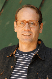 a man wearing glasses and a striped shirt is smiling for the camera