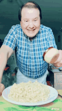 a man in a blue plaid shirt is pouring a slice of onion on a plate of macaroni and cheese