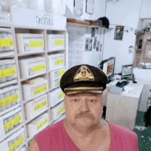 a man with a mustache is wearing a hat and a pink tank top in a room .