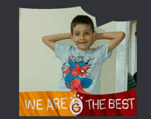 a boy wearing a spiderman shirt is standing in front of a banner that says we are the best