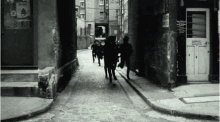 a black and white photo of people walking down a cobblestone street with a sign that says ' a ' on it