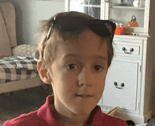 a young boy wearing sunglasses and a red shirt is looking at the camera .