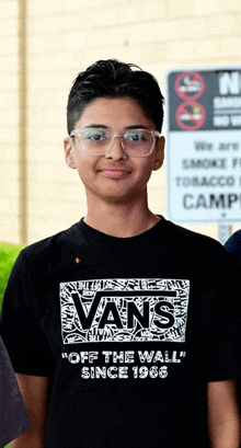 a young boy wearing glasses and a black vans off the wall shirt