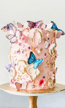 a pink cake decorated with butterflies and flowers is on a cake stand .