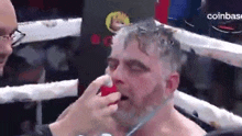 a man in a boxing ring with his eyes closed is getting his nose cleaned by another man .