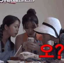 three women are sitting at a table looking at a cell phone and one has a tattoo on her arm