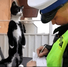 a police officer writes on a piece of paper while a black and white cat stands behind him