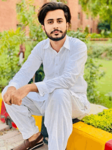 a man in a white shirt and pants sits on a yellow wall