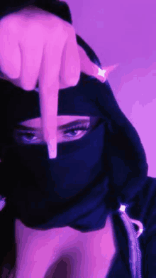 a woman wearing a niqab is giving the middle finger in a purple background .