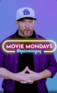 a man in a purple shirt stands in front of a movie mondays sign