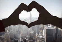 a person making a heart shape with their hands in front of a cityscape