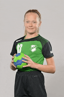 a young girl is holding a green and blue handball .