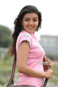 a woman in a pink shirt is smiling and carrying a purse