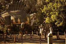 a statue of a dinosaur in a park with people standing around