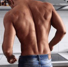 a shirtless man is standing in a kitchen with his hands on his hips .