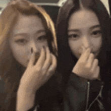 two girls are covering their noses with their hands .