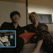 two people sitting on a couch with a picture of a man driving a car in the background