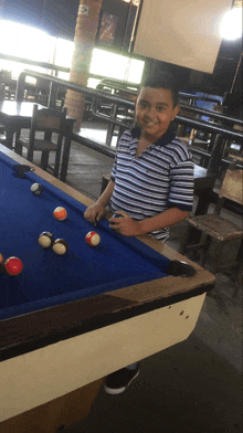 a boy in a striped shirt is playing pool and smiling