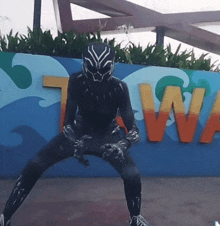 a man in a black panther costume is squatting in front of a sign that says tawa