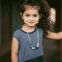 a little girl wearing a blue shirt and a necklace smiles