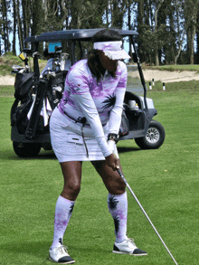 a woman is swinging a golf club on a golf course in front of a golf cart