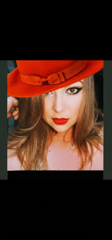 a woman wearing an orange hat and red lipstick looks at the camera