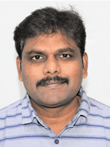 a man with a mustache wearing a striped shirt looks at the camera