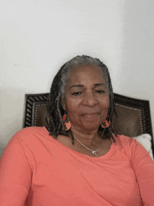 a woman with dreadlocks wearing a pink shirt and earrings