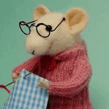 a stuffed mouse wearing glasses and a pink sweater is holding a blue and white checkered towel .