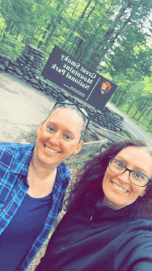 two women are posing for a picture in front of a sign that says " national park service " on it