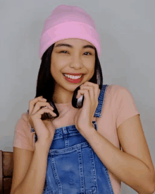 a woman wearing overalls and a pink beanie smiles