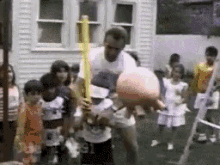 a man is holding a bat and a basketball in front of a group of children including one with the number 91 on his shorts