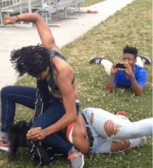 a man is laying on the grass taking a picture of two women fighting