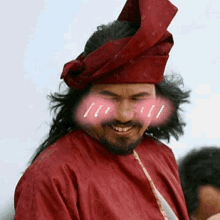 a man with a beard wearing a red shirt and a red turban is smiling .