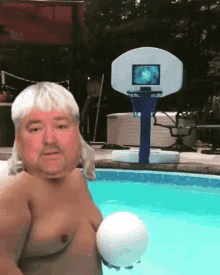 a shirtless man holds a volleyball in front of a basketball hoop in a pool