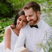 a bride and groom are reading a book together in a garden .