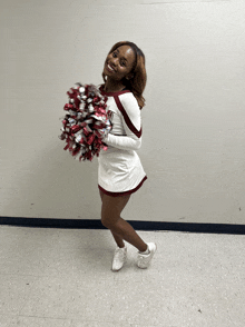 a cheerleader in a maroon and white uniform holds a pom pom with the letter t on it